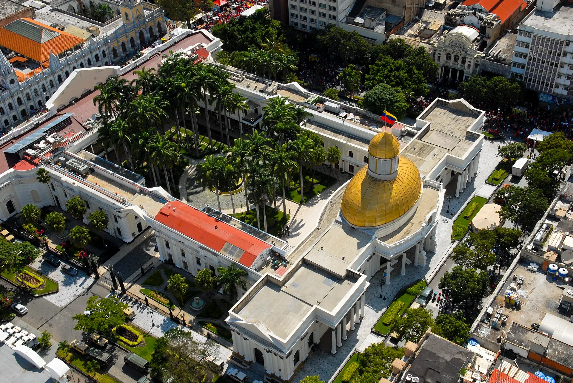 Aerial view of the Federal Legislative Palace in Caracas, with its golden dome, palm-filled courtyard and white wings.