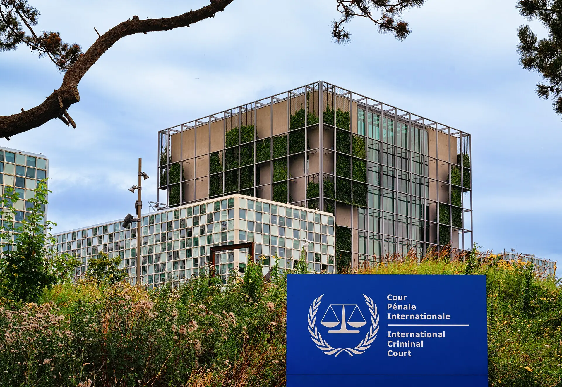 Blue sign reading 'Cour Pénale Internationale – International Criminal Court' in front of the ICC building in The Hague.